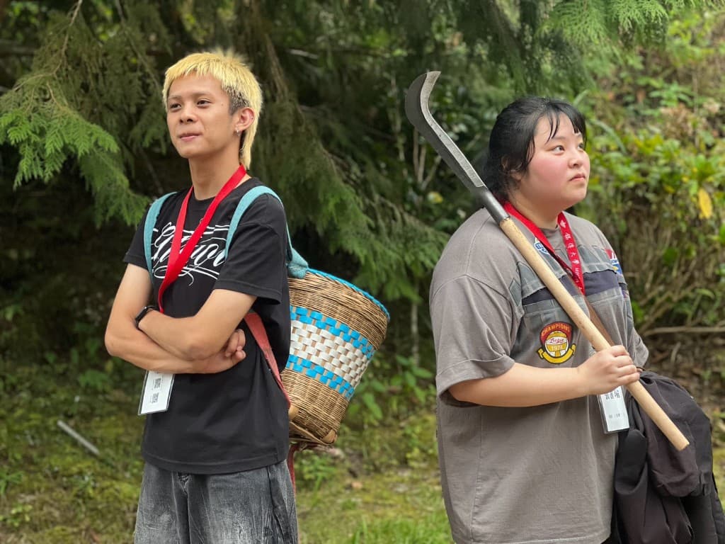 兩位學生分別背著竹簍、拿著山刀,站在山林步道旁